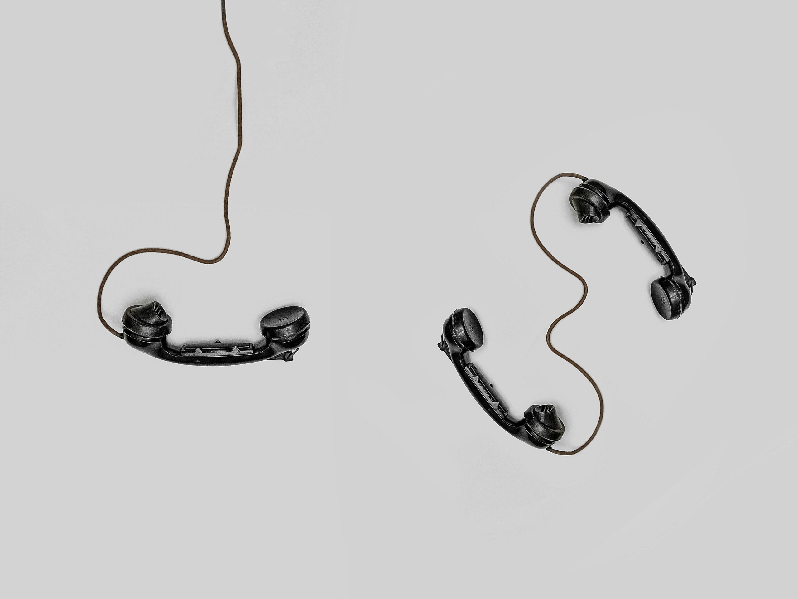 Two vintage black telephone handsets connected by cords on gray background.